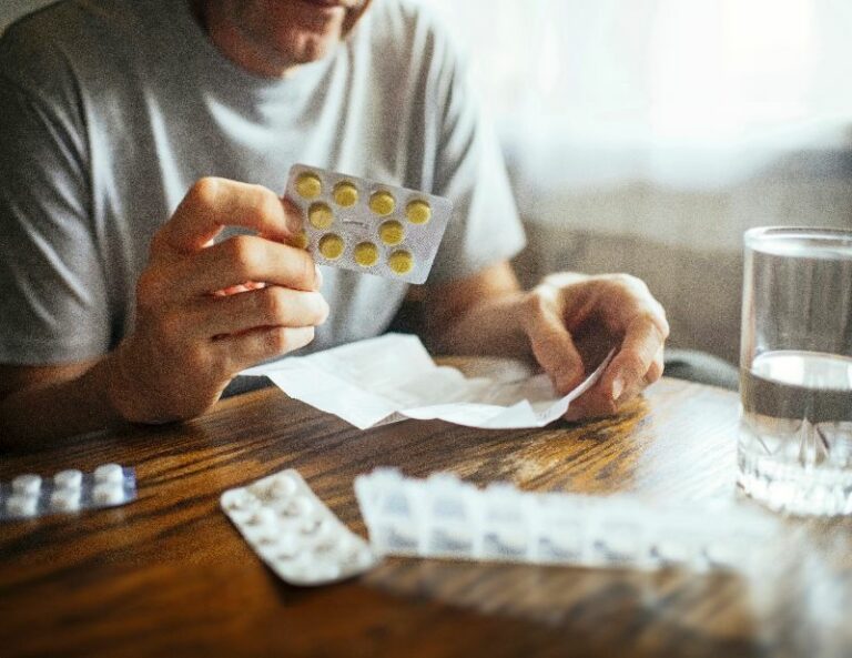 Mies lukee lääkkeen pakkausselostetta ja miettii lääkkeiden haittavaikutuksia.