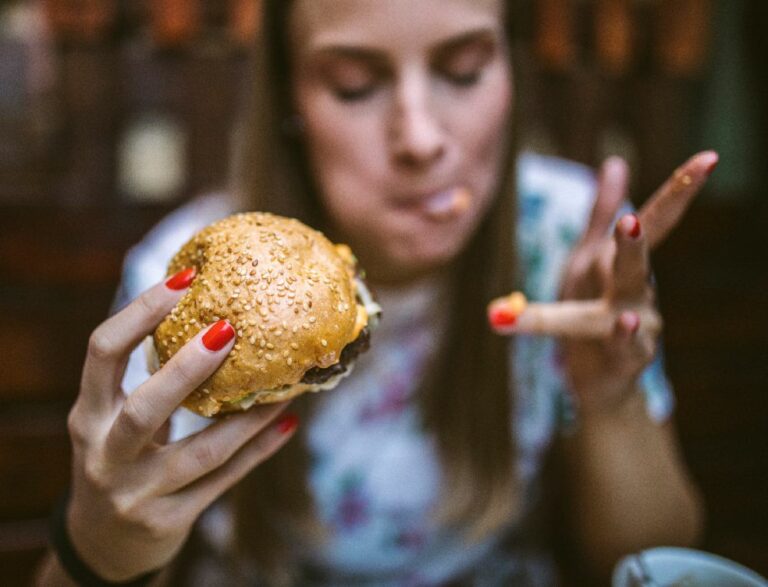 Nainen herkuttelee hampurilaisella, mikä voi aiheuttaa ärtyvän suolen oireyhtymästä kärsivälle vatsavaivoja.